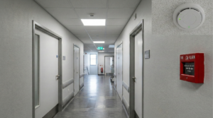 Manual call point and smoke detector in a corridor showing UK fire alarm category basics